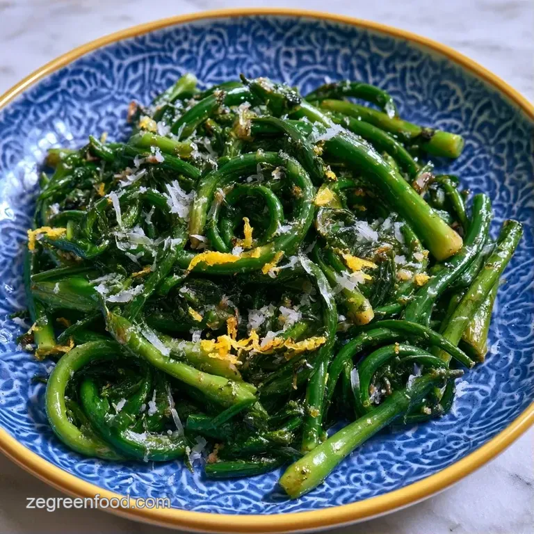Tender green garlic shoots dusted with toasted parmesan cheese served on a white ceramic plate with lemon wedges.